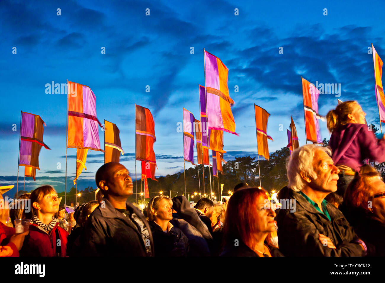 I frequentatori del festival al tramonto a WOMAD 2011, Charlton Park di Malmesbury, Wiltshire, Inghilterra, Regno Unito con il flag di tipo iconico in background Foto Stock