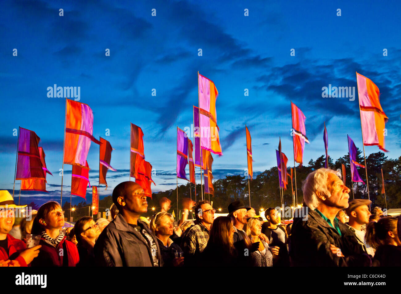I frequentatori del festival al tramonto a WOMAD 2011, Charlton Park di Malmesbury, Wiltshire, Inghilterra, Regno Unito con il flag di tipo iconico in background Foto Stock