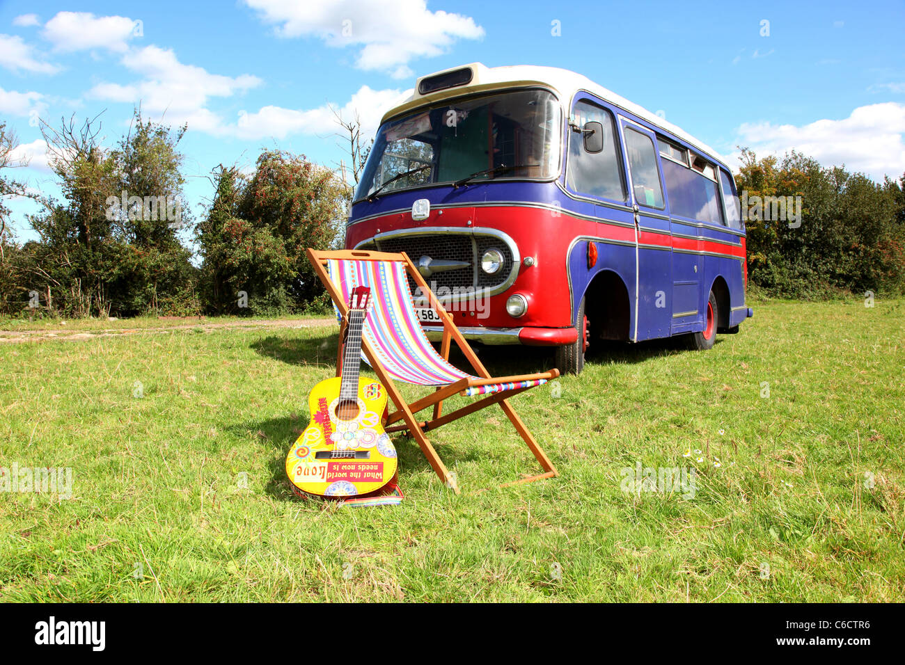 1971 Bedford camper parcheggiato in un campo con una chitarra acustica e una sedia a sdraio in primo piano. Foto Stock