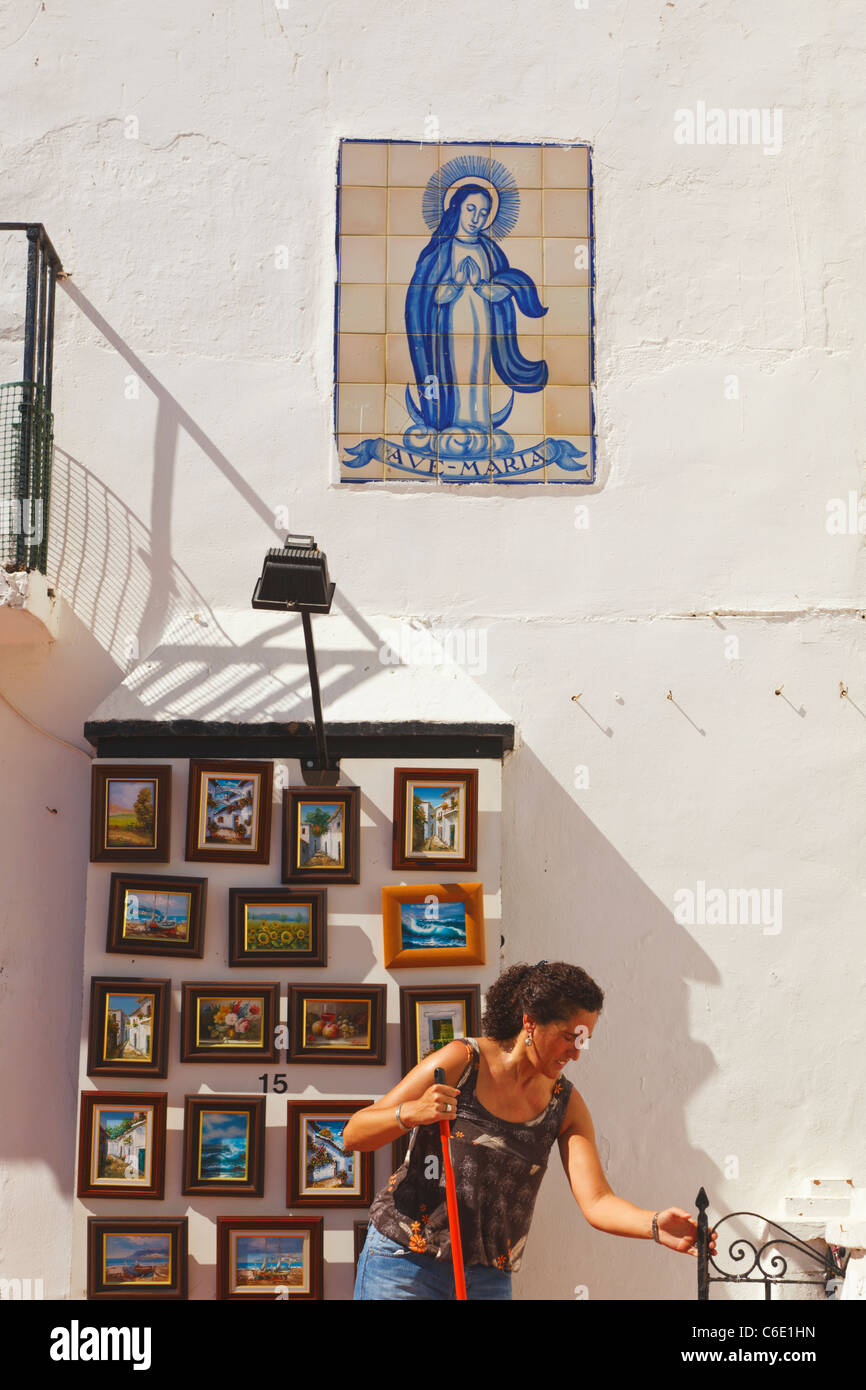 Donna che spazzava di fronte a un negozio di souvenir che vende dipinti. Torremolinos, Provincia di Malaga, Costa del Sol, Spagna. Foto Stock
