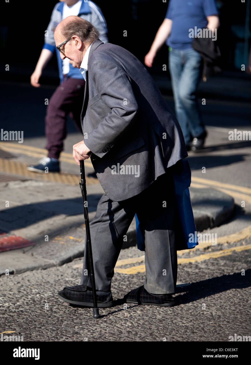 Pedone anziano che attraversa la strada con bastone da passeggio, Londra, Inghilterra, Regno Unito. Foto Stock