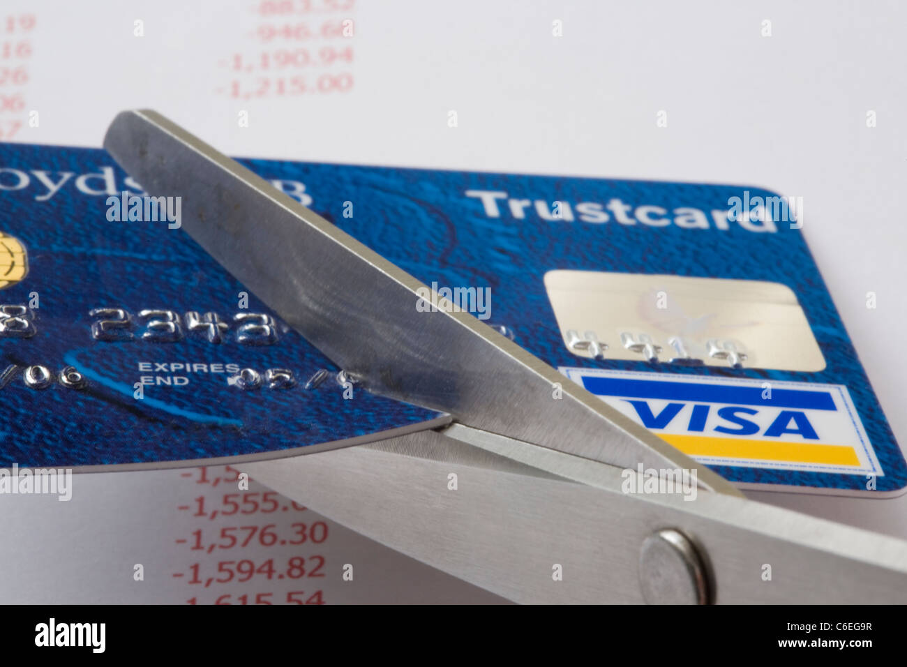 Un paio di forbici il taglio di una carta di credito Visa in stretta fino al di sopra di un foglio di conti che mostra i debiti in rosso. Inghilterra, Regno Unito, Gran Bretagna Foto Stock