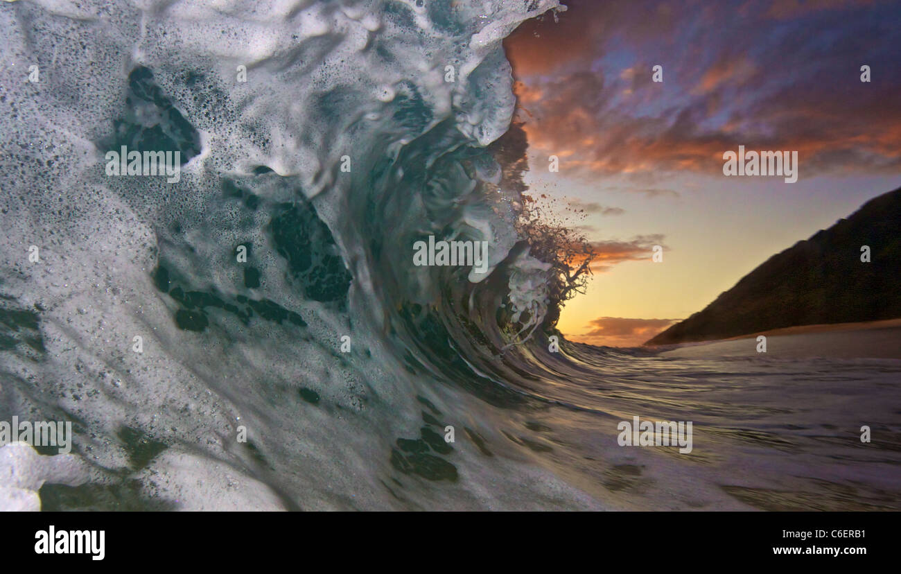 Caldo tramonto con un onda di schiantarsi su una spiaggia segreta. Foto Stock