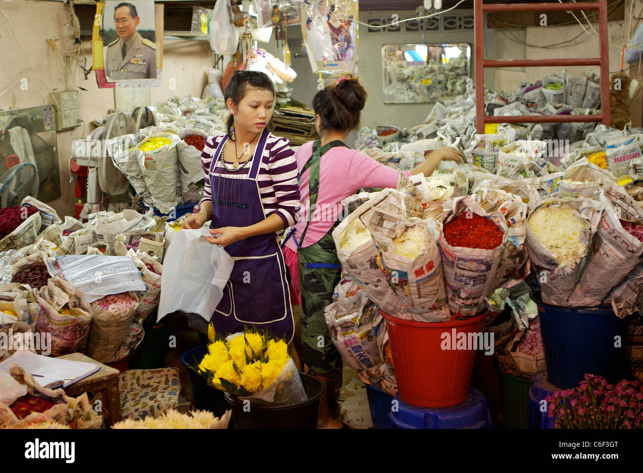 Due donne che lavorano in un fiore di avvolgimento di stallo le rose e i crisantemi nel Pak Klong Talat mercato (mercato dei fiori) di Bangkok Foto Stock