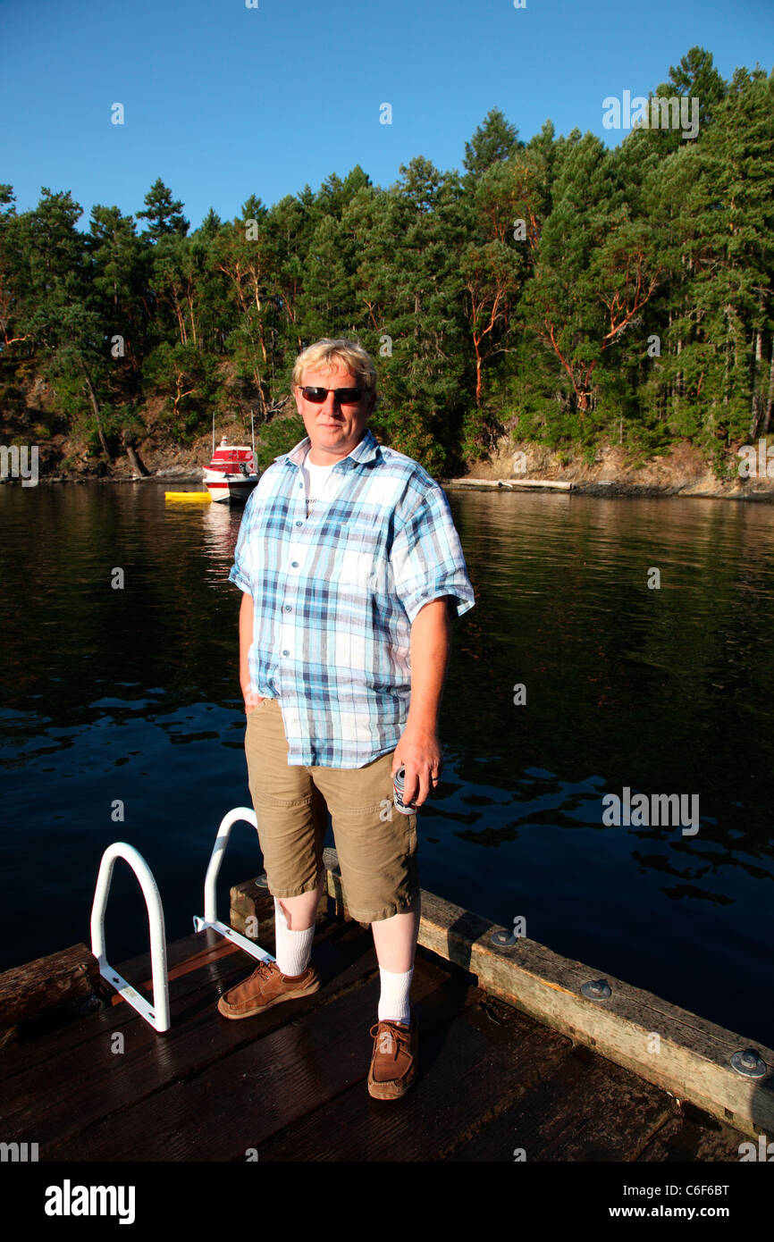 Uomo in piedi sul dock dall'oceano su Portland isola in un pomeriggio soleggiato. Garry querce e corbezzoli dietro di lui. Foto Stock