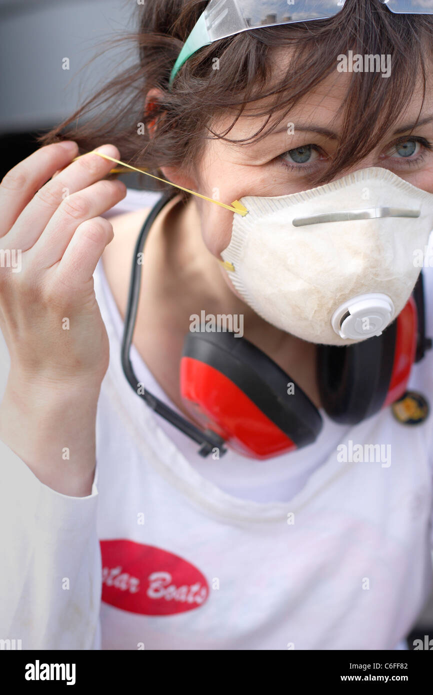 Una giovane donna mettendo su una maschera per il viso e le cuffie di protezione e occhiali di sicurezza per la protezione durante il lavoro. Foto Stock