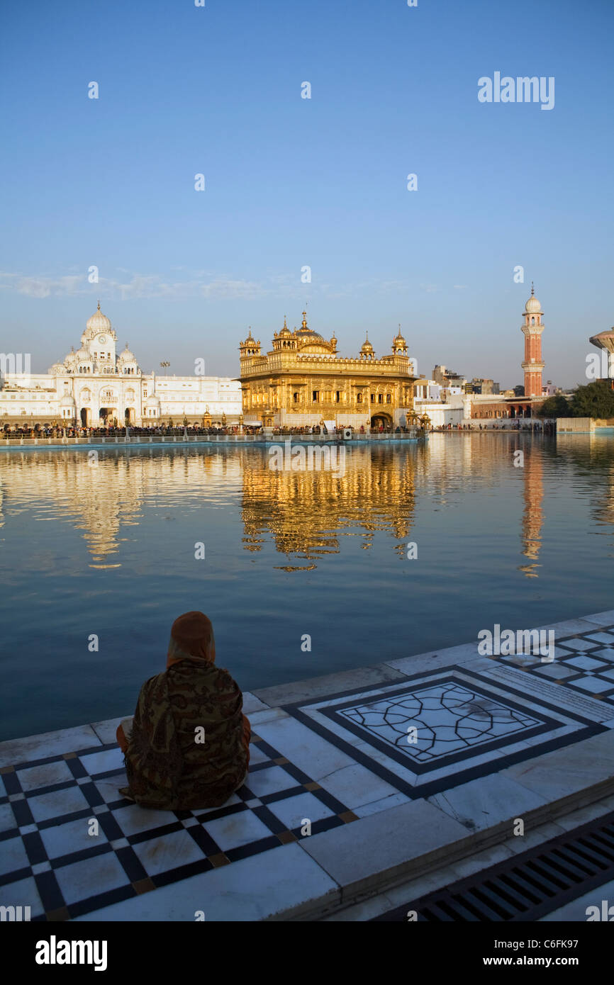 Un devoto si siede sul bordo del piccolo lago che circonda il XVI secolo la religione Sikh Tempio d'oro di Amritsar, stato del Punjab, India Foto Stock