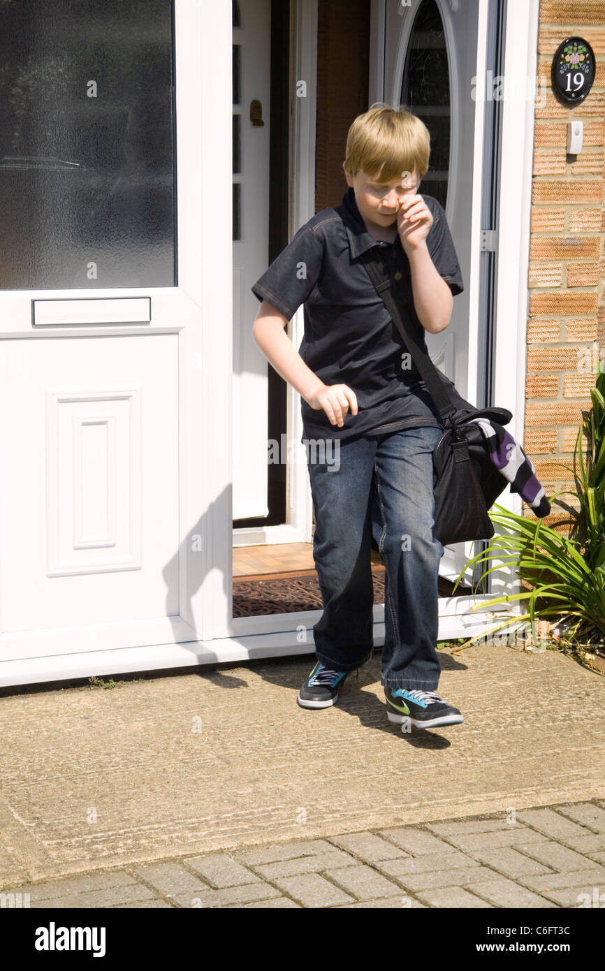 Un dodicenne ragazzo corre gridando da una casa con una fretta sacchetto confezionato Foto Stock