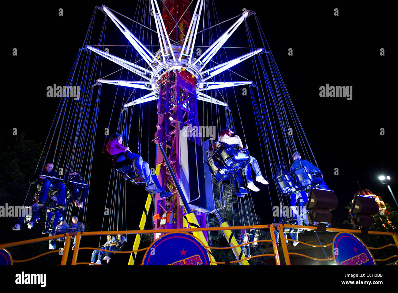 La gente seduta su una illuminazione fairground ride di notte. Foto Stock