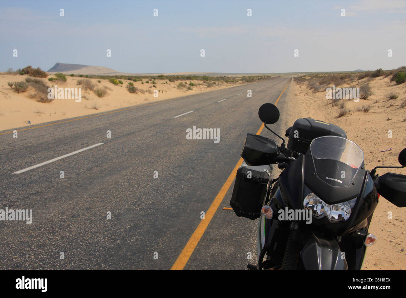 Touring bike parcheggiato a fianco di un lungo rettilineo di tar strada che corre attraverso il paesaggio del deserto Foto Stock