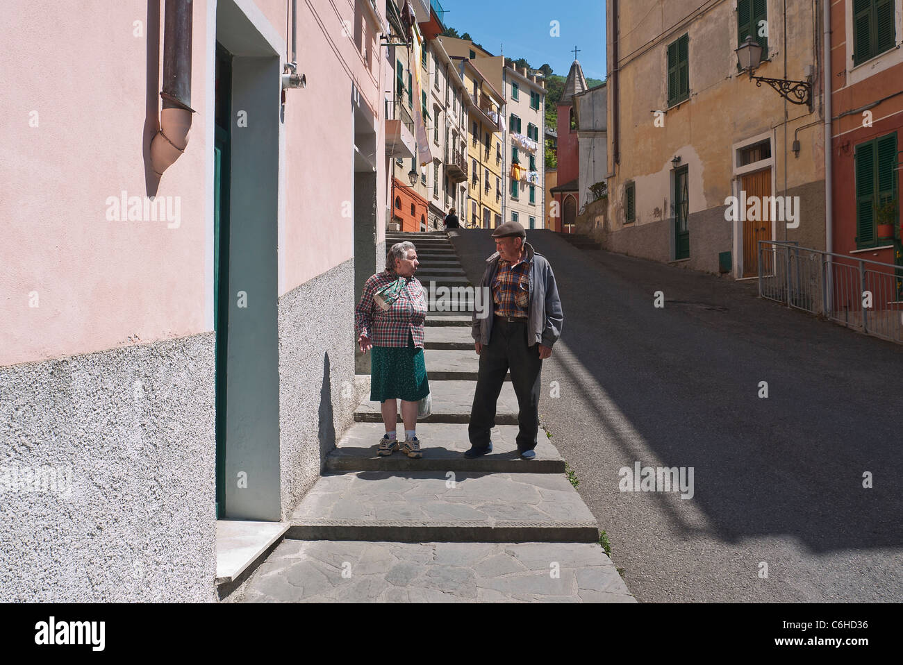 Un anziana coppia italiana parla e gesto come essi camminare sul marciapiede nel loro villaggio di Riomaggiore, Cinque Terre, Italia. Foto Stock