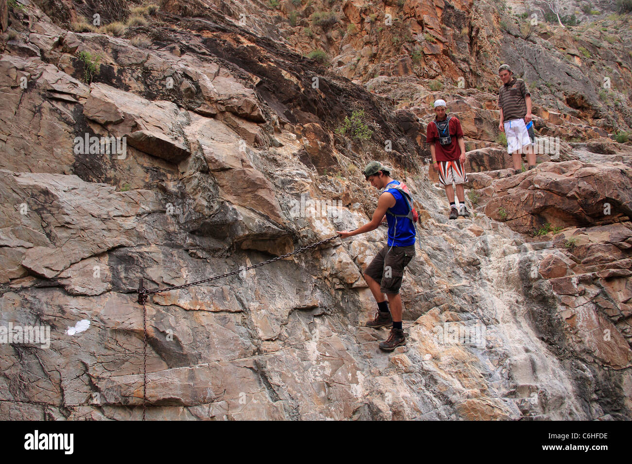 Tre escursionisti attraversante ripida roccia utilizzando catene Foto Stock