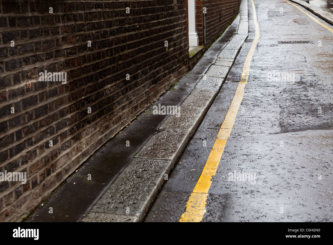 Linea gialla singola e un muro di mattoni su una strada strada bagnata, vicino Chancery Lane, Londra Foto Stock
