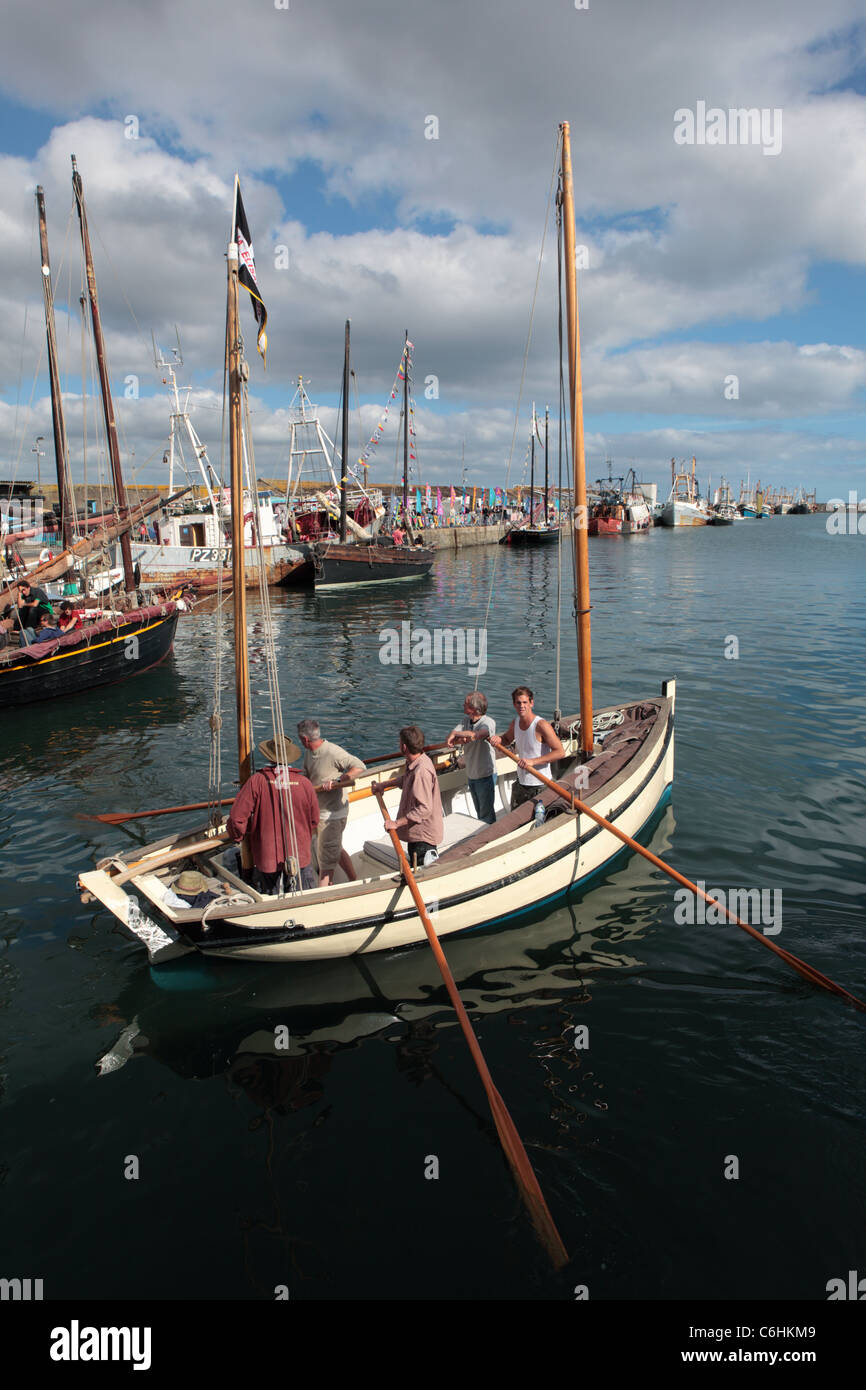 Una piccola barca a vela con gli uomini a remi nel Porto di Newlyn, Cornwall Foto Stock