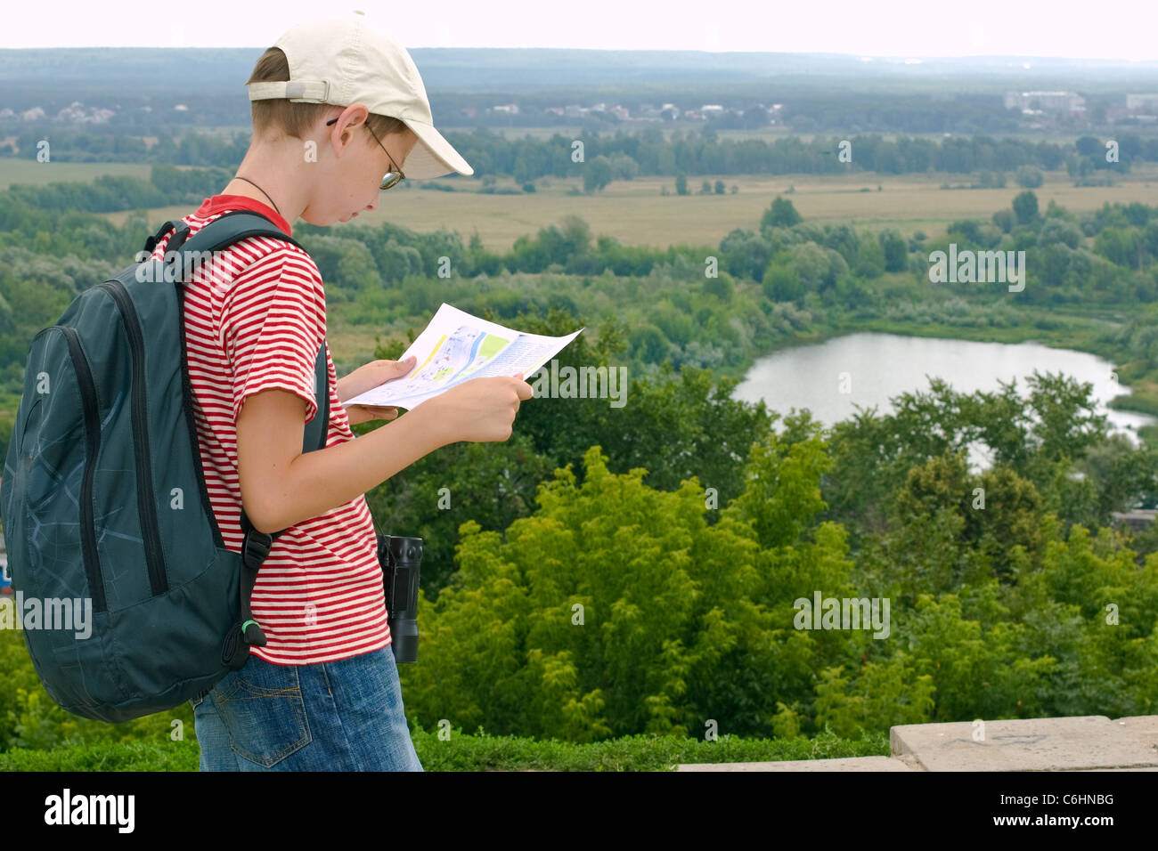 Ragazzo con il binocolo e zaino guarda la mappa su una escursione Foto Stock
