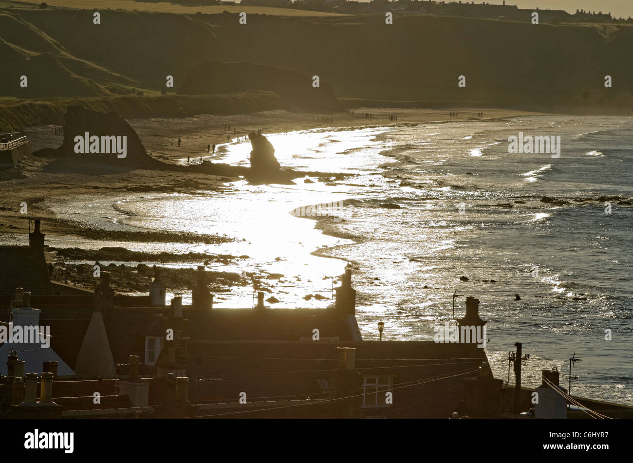 Cullen Beach- Moray Coast in fine di sun con rock e case in profilo Foto Stock