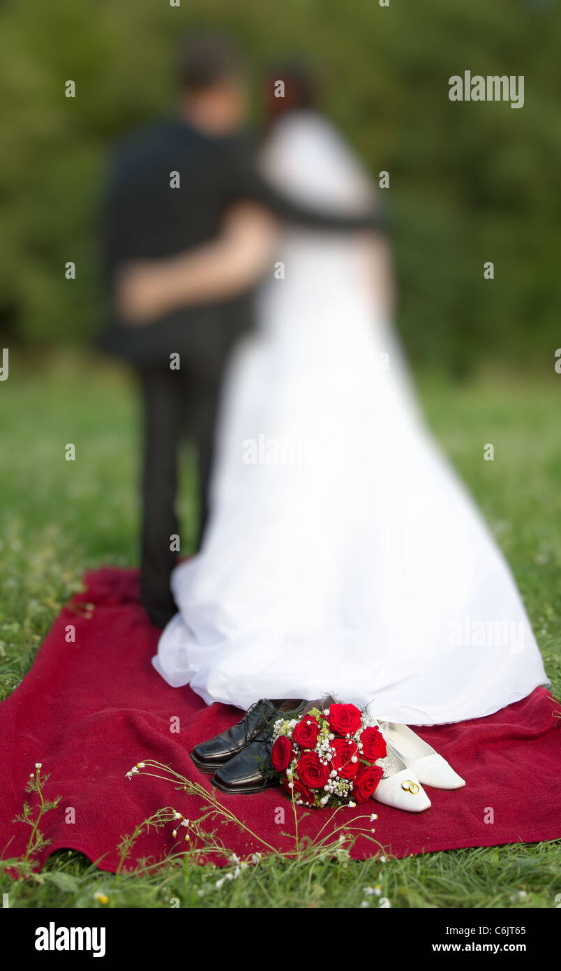 Simbolo di nozze concetto con nuziale bianco scarpe da ballo a rose rosse bouquet nuziale e due intrecciano golden gli anelli di nozze Foto Stock