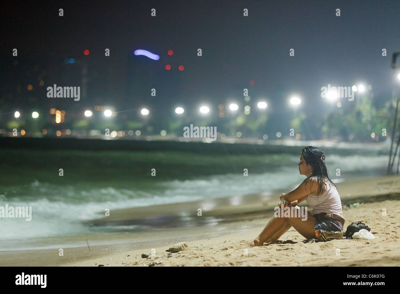 Donna thai indossando vestiti bagnati seduto sulla sabbia in spiaggia di Pattaya di notte, Pattaya , Thailandia Foto Stock