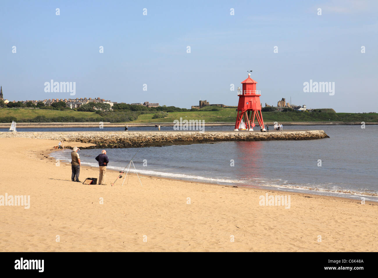Due uomini la pesca da allevamento o sabbia spiaggia Littlehaven, Groyne faro in background a South Shields, North East England, Regno Unito Foto Stock