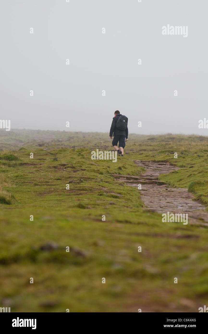 Un camminatore solitario ascende Pen-y-ventola in Brecon Beacons sotto basse nubi Foto Stock