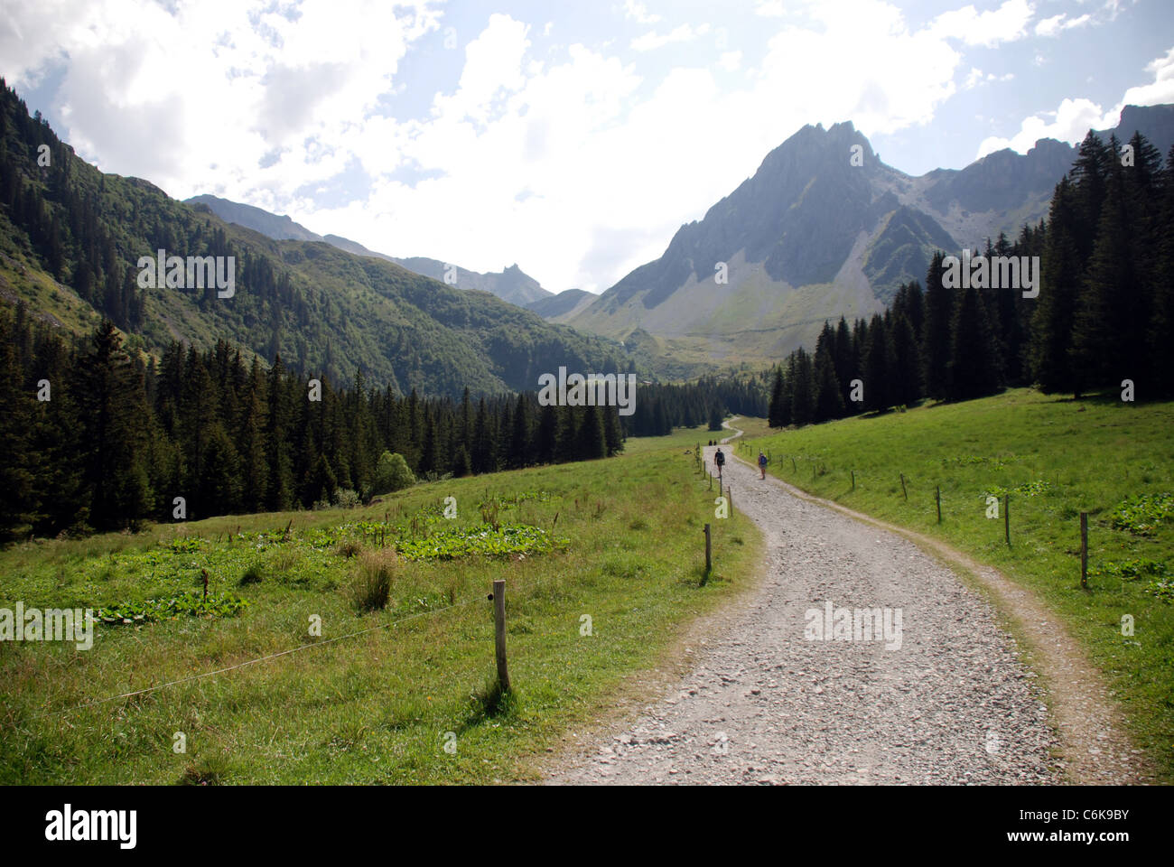 Una strada di montagna si snoda attraverso una valle nelle alpi francesi con le alte montagne sullo sfondo Foto Stock
