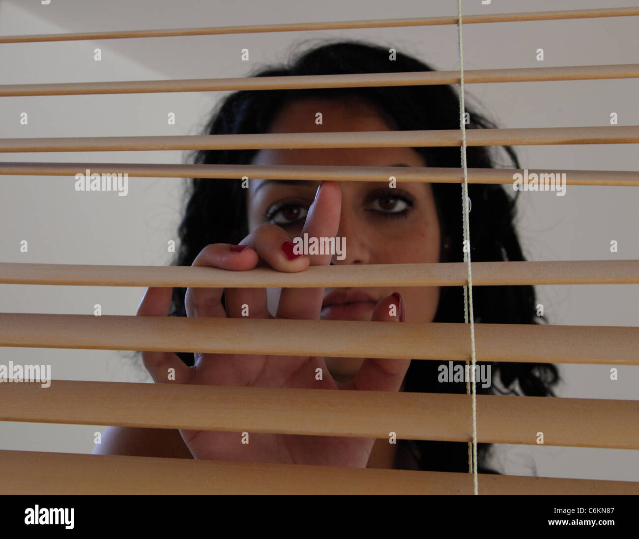 Apertura di donna e guardando attraverso i ciechi di legno. Foto Stock