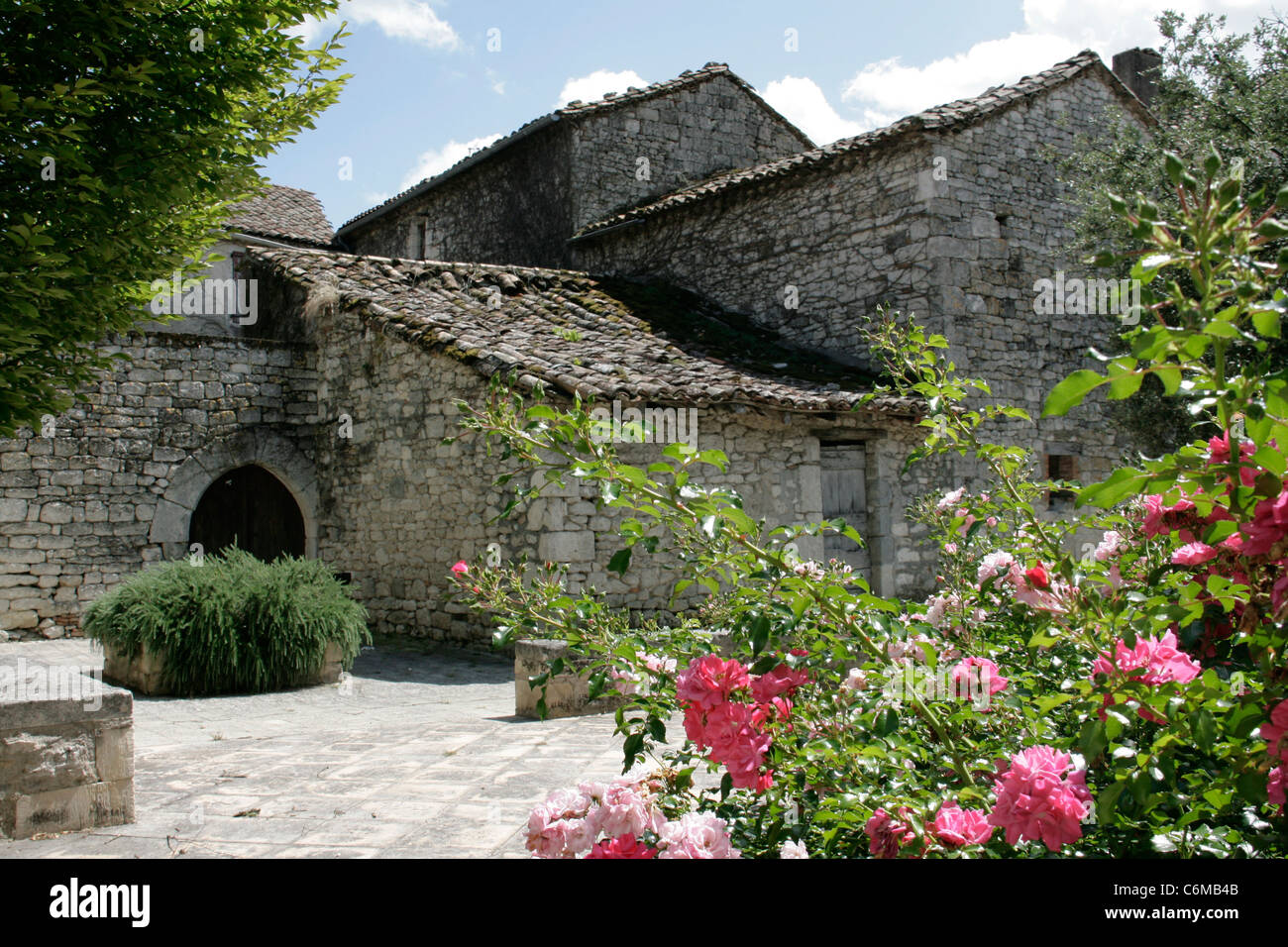 Le stalle e gli edifici realizzati in pietra naturale in francese borgo rurale con arco e rose in primo piano Foto Stock