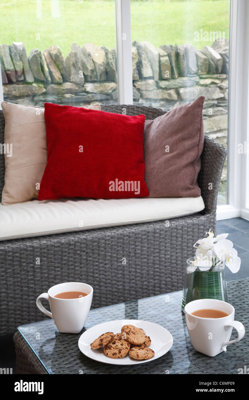 Bollitore per tè o caffè e biscotti in una veranda con sedie di rattan e interni dal design moderno Foto Stock