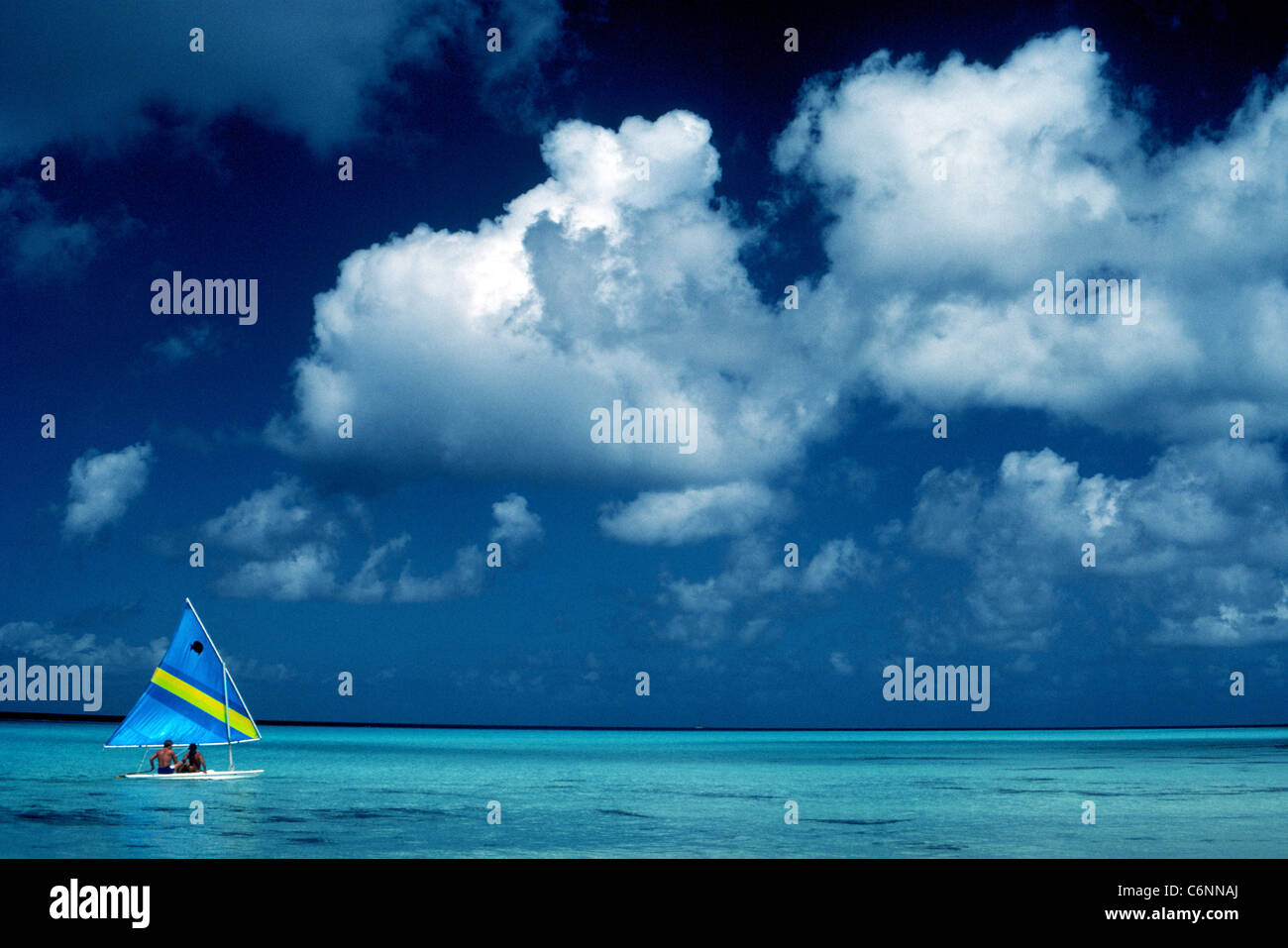 Una piccola barca a vela con due vacanzieri scorre attraverso il turchese del Mare dei Caraibi sotto puffy nuvole bianche e un vivid blue sky a Cozumel, Messico. Foto Stock