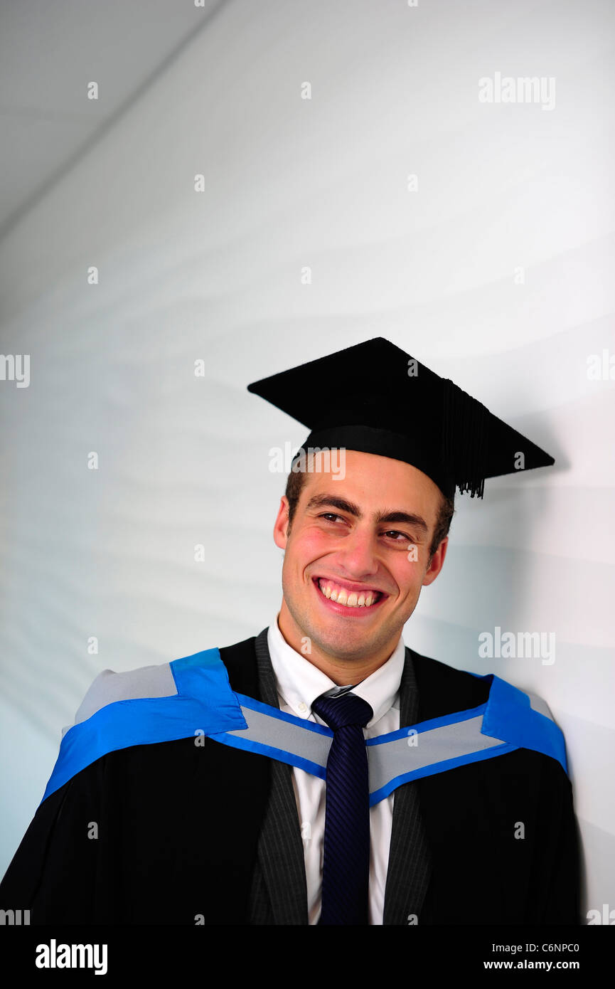 Un sorridenti laureati maschi nel cappuccio e camice in Università sul giorno di graduazione Foto Stock