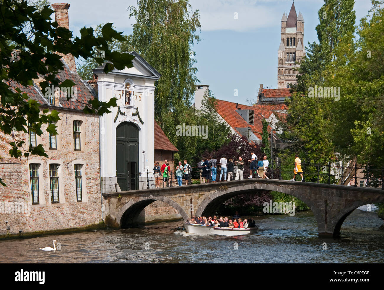 Bruges (Brugge) canal con Swan e la barca turistica a bridge e alla porta al beghinaggio (Prinselijke Begijnhof van Wijngaerde) Foto Stock