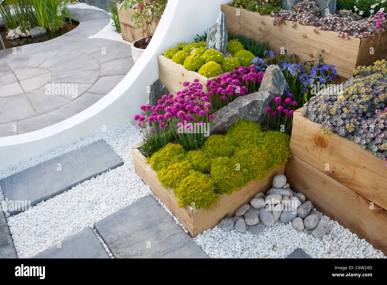 Un moderno giardino con patio circolare in pietra pavimentata e letti rialzati realizzati con traversine in legno vecchie piante alpine in container UK Foto Stock