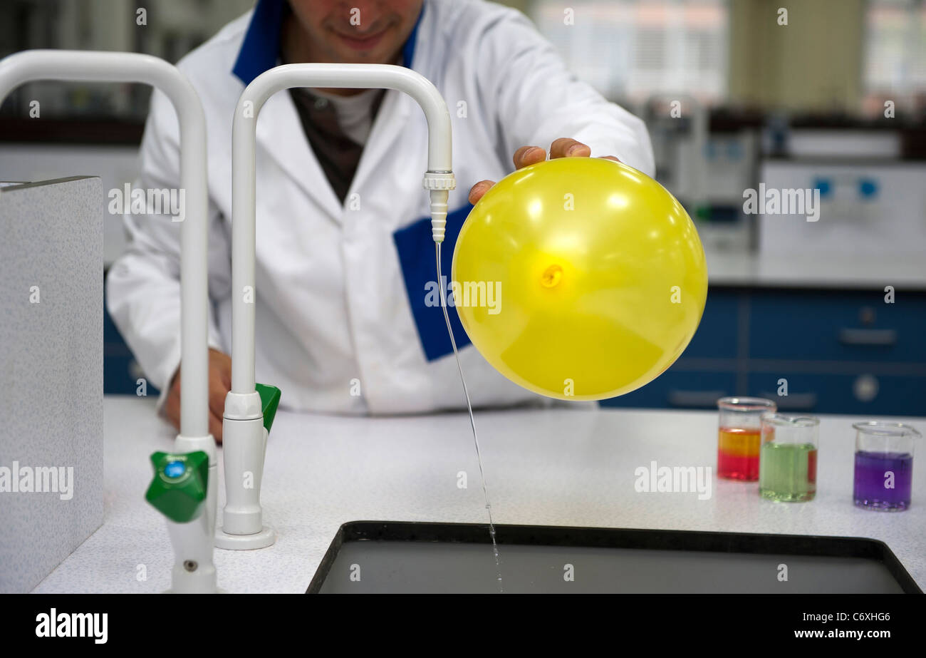 Un insegnante di scienze si piega di acqua da un rubinetto utilizzando statico dal un palloncino. Foto Stock