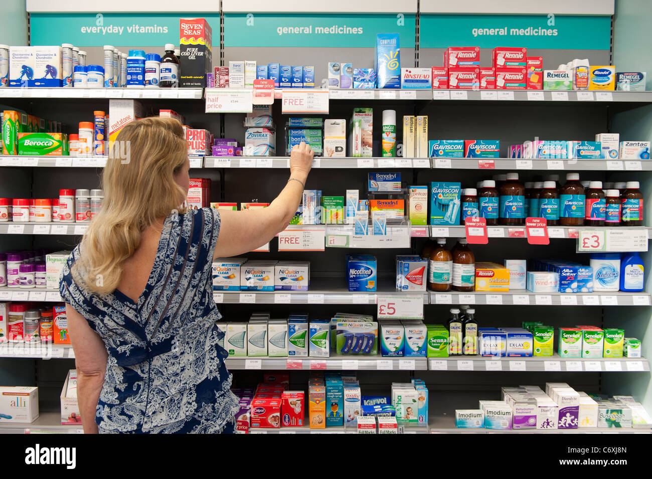 Una donna raggiunge per i medicinali su uno scaffale in una farmacia del Regno Unito. Foto Stock