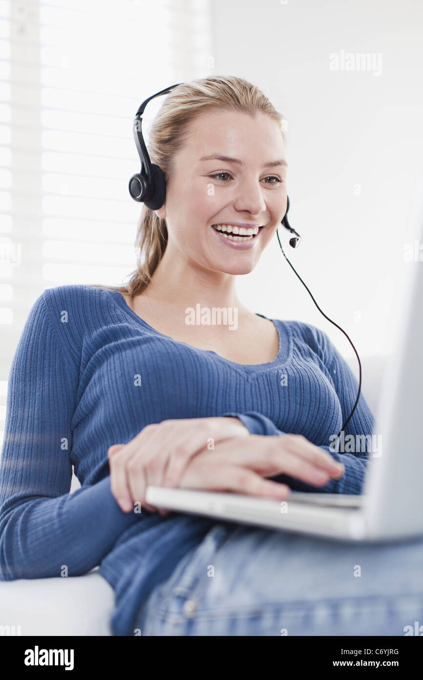 Donna che utilizza la cuffia sul computer portatile Foto Stock