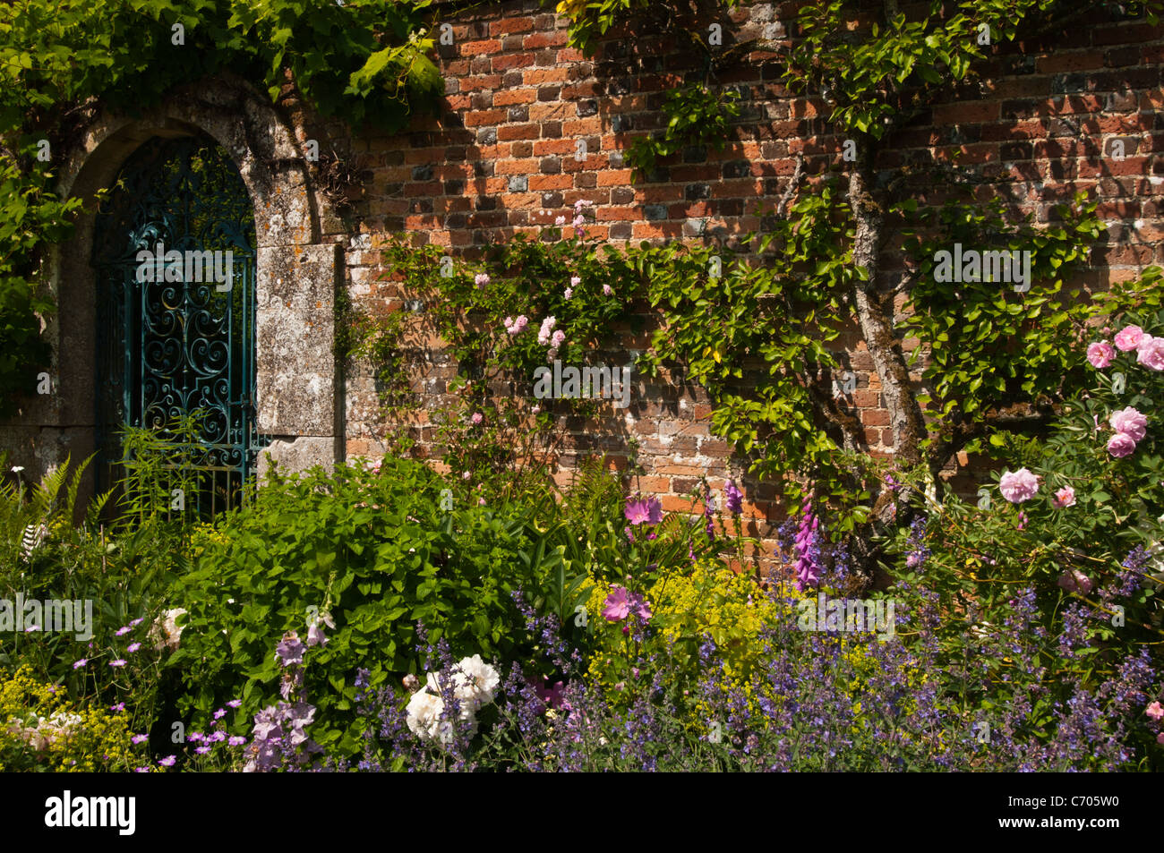 Colorate confine erbacee accanto a un ornato cancellata in ferro battuto entro il giardino murato di Rousham House, Oxfordshire, Inghilterra Foto Stock