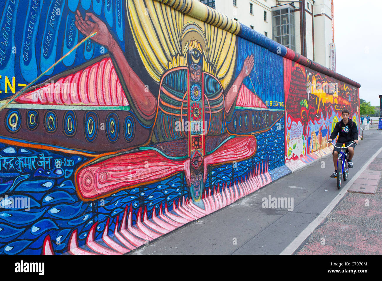 La parte restante pezzo dipinto del muro di Berlino in Germania uomo ragazzo ciclo di bicicletta pedalando attraverso il colore colorato colorato Foto Stock
