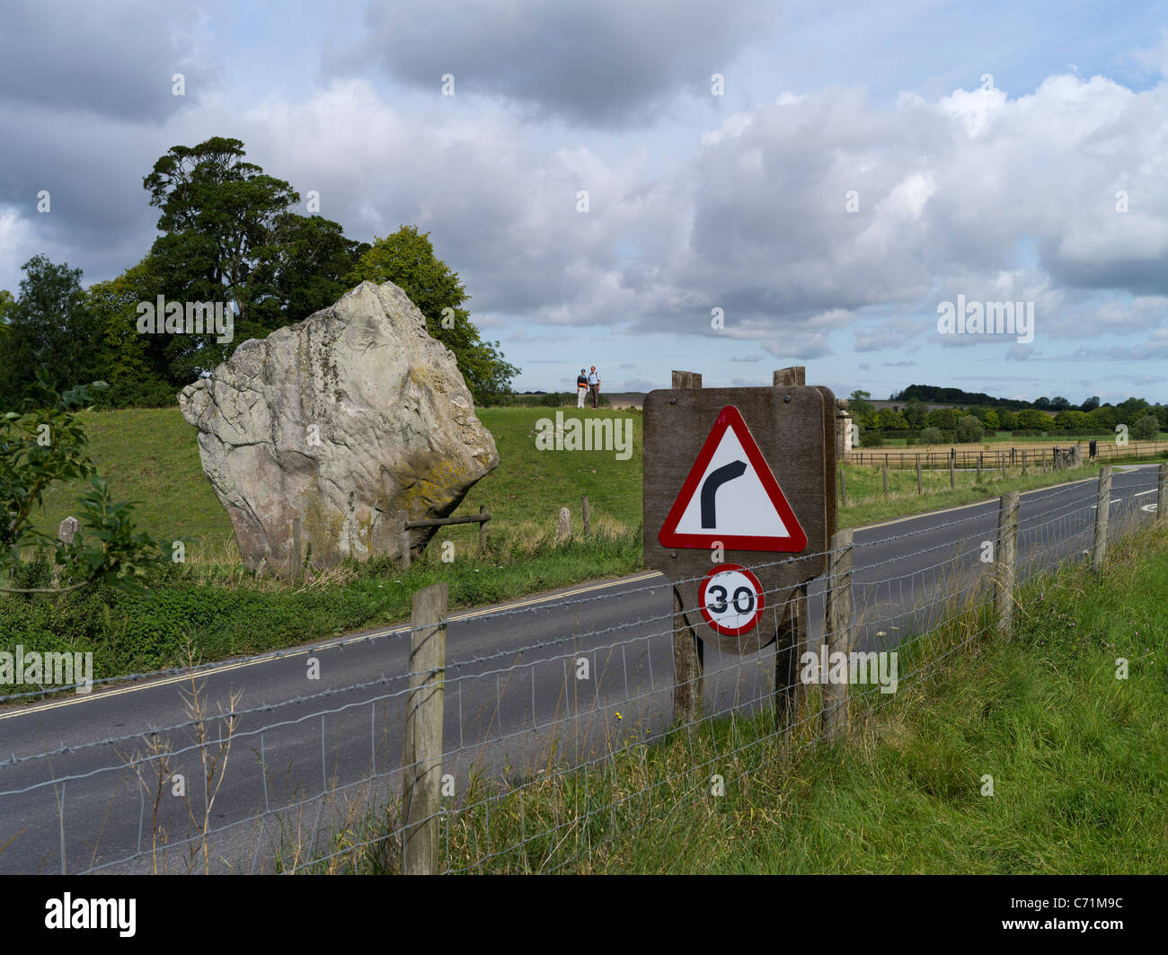 dh Avebury Stone Circle AVEBURY WILTSHIRE turisti che guardano il singolo neolitico in piedi pietra e segnaletica stradale Foto Stock