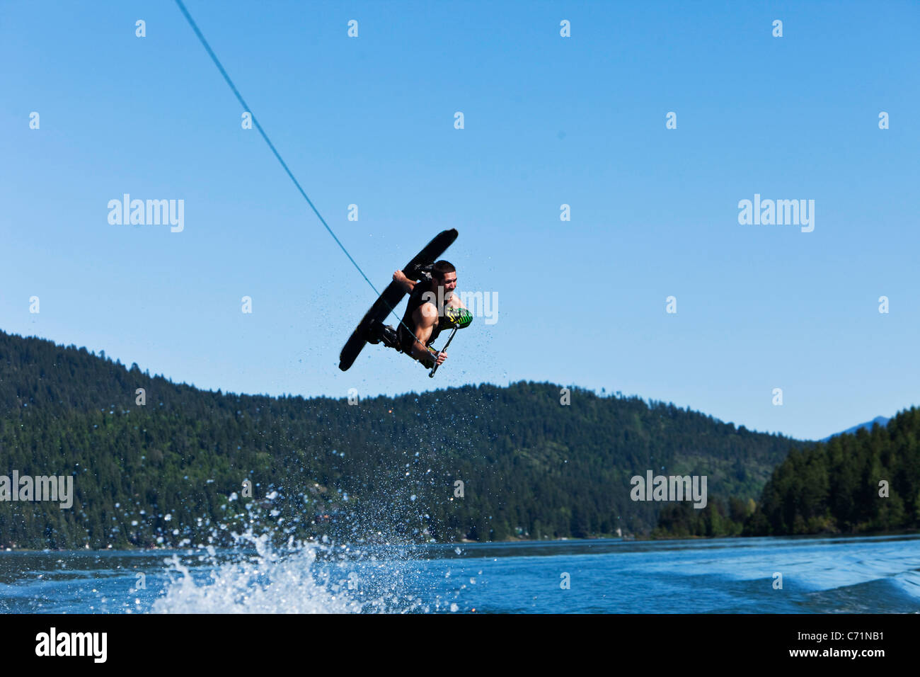 Un uomo atletico wakeboard salti enormi sopra la scia e le montagne in Idaho. Foto Stock