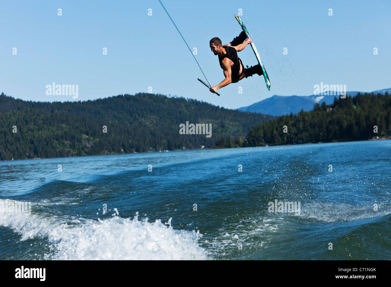 Un uomo atletico wakeboard salti enormi sopra la scia e le montagne in Idaho. Foto Stock