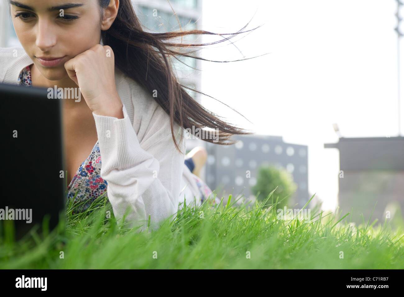 Giovane donna sdraiata su stomaco sull'erba con i capelli soffiando nel vento Foto Stock
