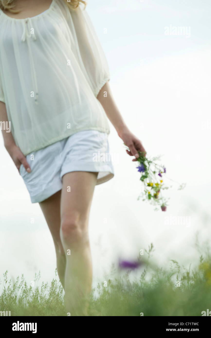 Giovane donna camminare nel prato, trasportare bouquet di fiori selvatici, ritagliato Foto Stock