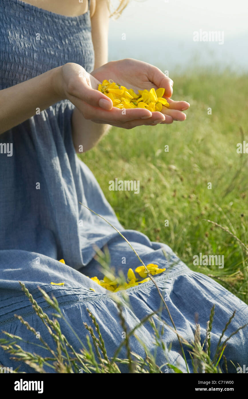 Giovane donna in ginocchio di prato, azienda di petali di fiori in mani, ritagliato Foto Stock