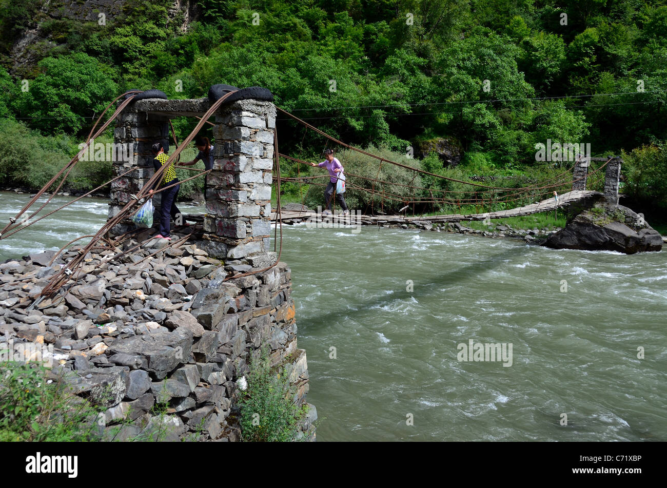 Donne cross un primitivo ponte sospeso attraverso un insidioso fiume. Sichuan, in Cina. Foto Stock