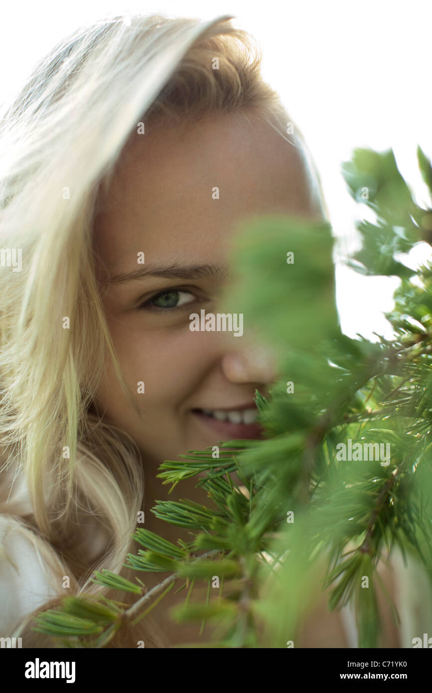 Sorridente giovane donna dietro i rami degli alberi, ritagliato Foto Stock