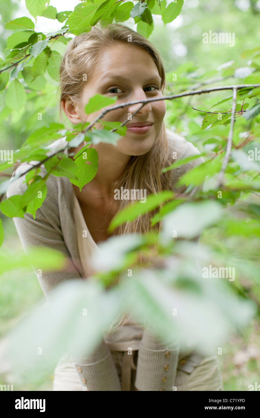 Giovane donna dietro i rami degli alberi Foto Stock