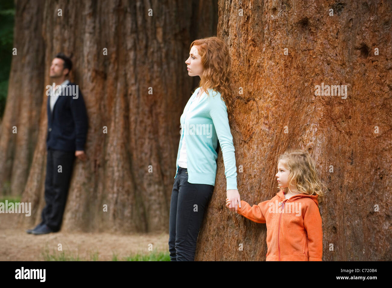 Madre e figlia appoggiata ad albero, padre separato permanente in background Foto Stock