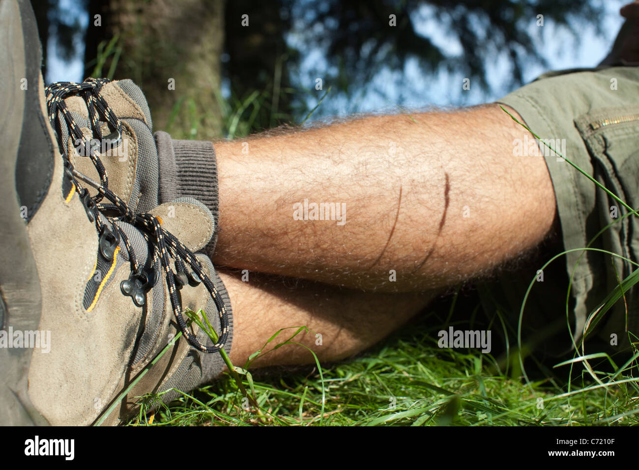Uomo in scarpe da trekking rilassante sull'erba con le gambe incrociate, sezione bassa Foto Stock
