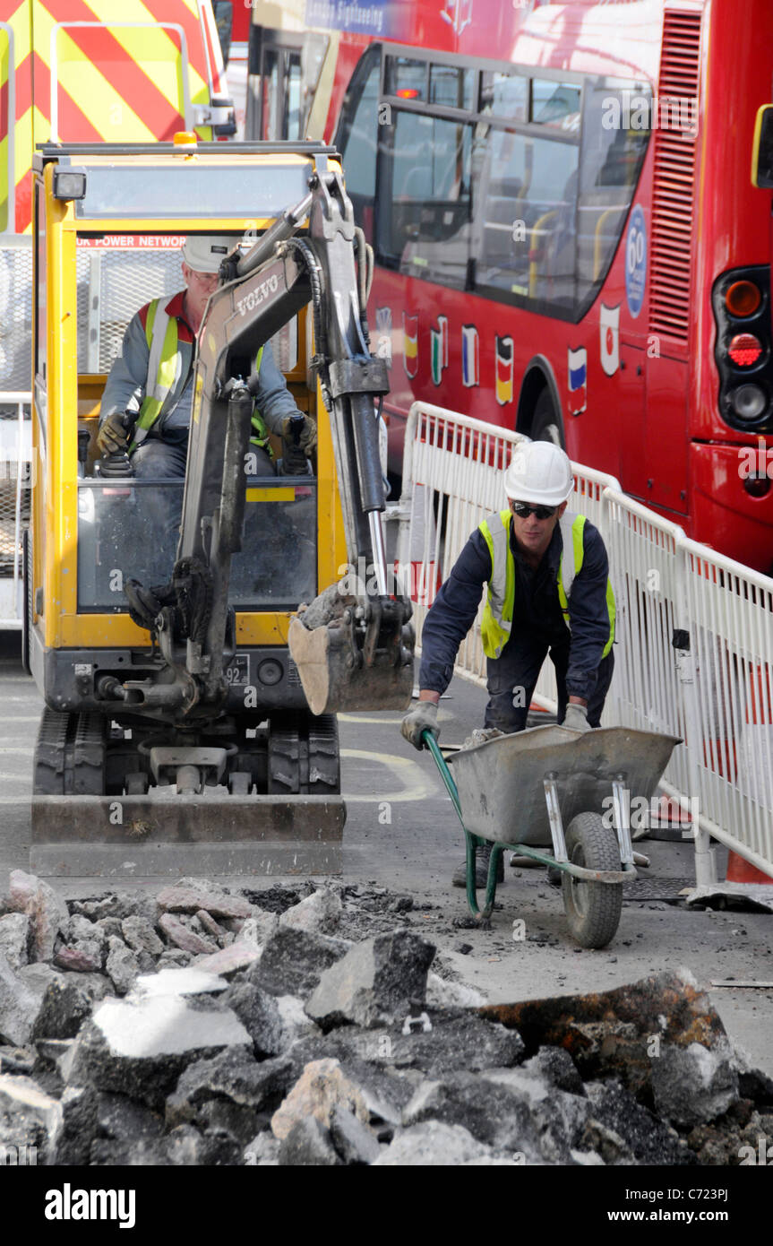 Lavoratori con vista aerea e miniescavatore che lavorano su lavori stradali nella corsia degli autobus accanto al traffico di rosso doppio pianista Autobus Regent Street West End Londra UK Foto Stock