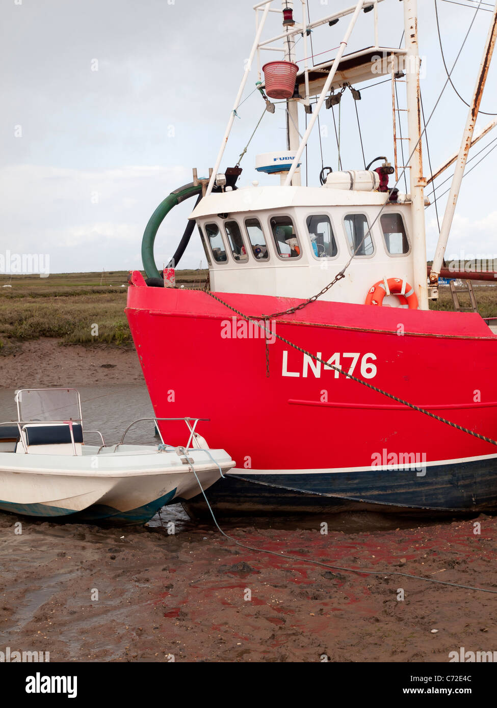 Rosso barca da pesca giacente sul fango a bassa marea Brancaster Staithe Norfolk in un giorno di pioggia Foto Stock
